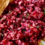 Cranberry Ginger Lime Salsa with tortilla chips, fresh cilantro and lime wedges in a terracotta bowl